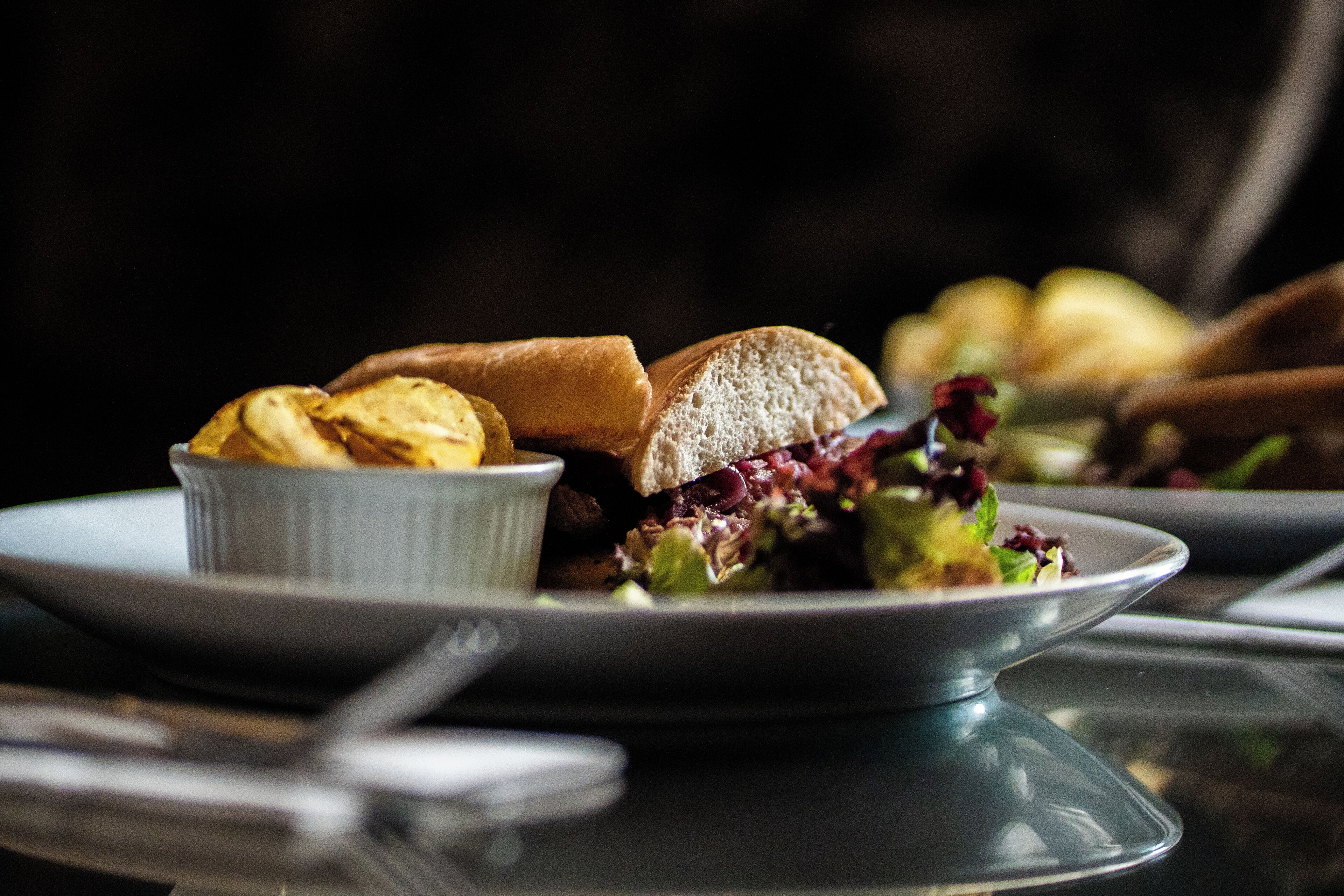 A plate with a sandwich, chips, and a small bowl of salad.