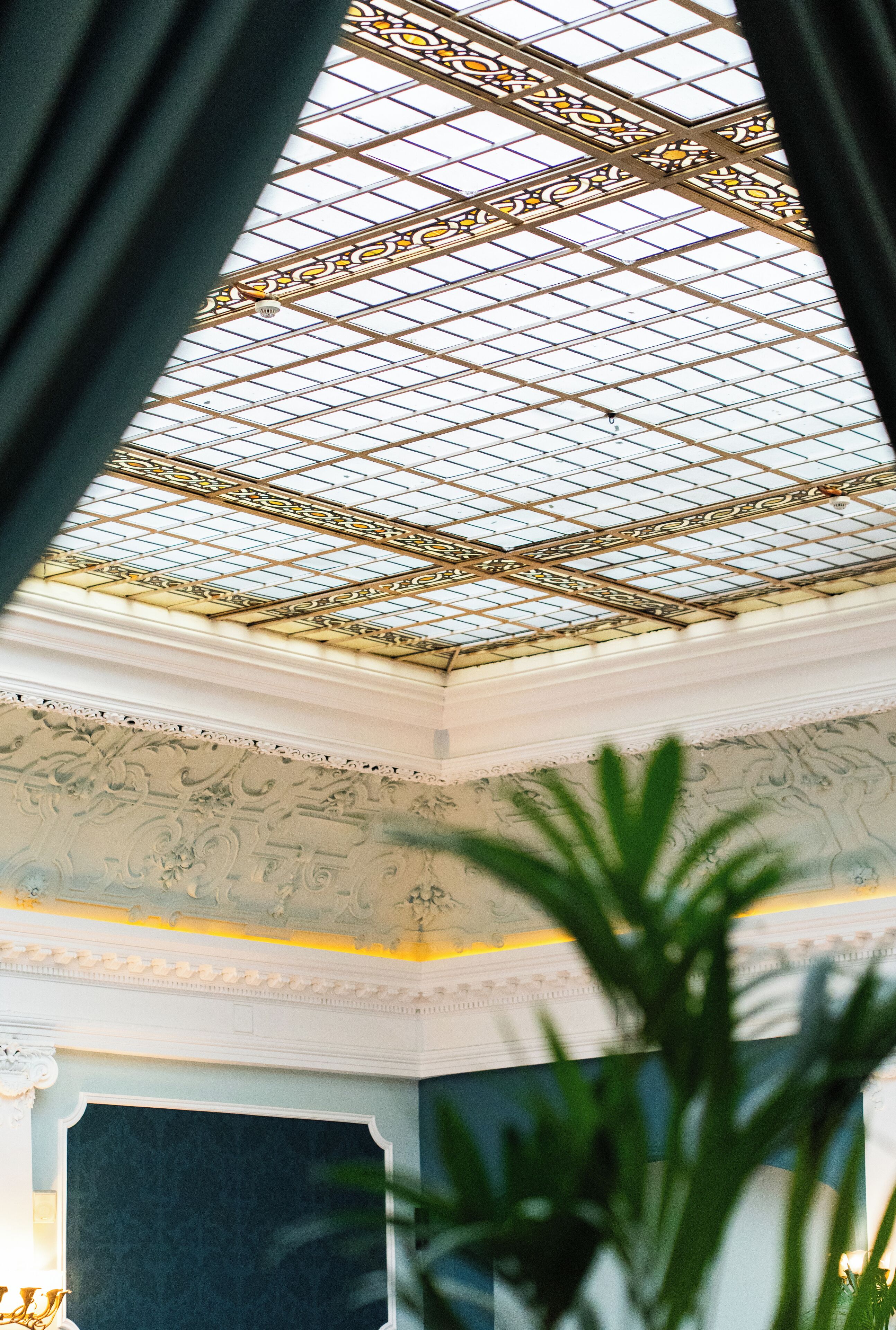 A room with a high ceiling featuring a glass skylight and ornate ceiling decorations.