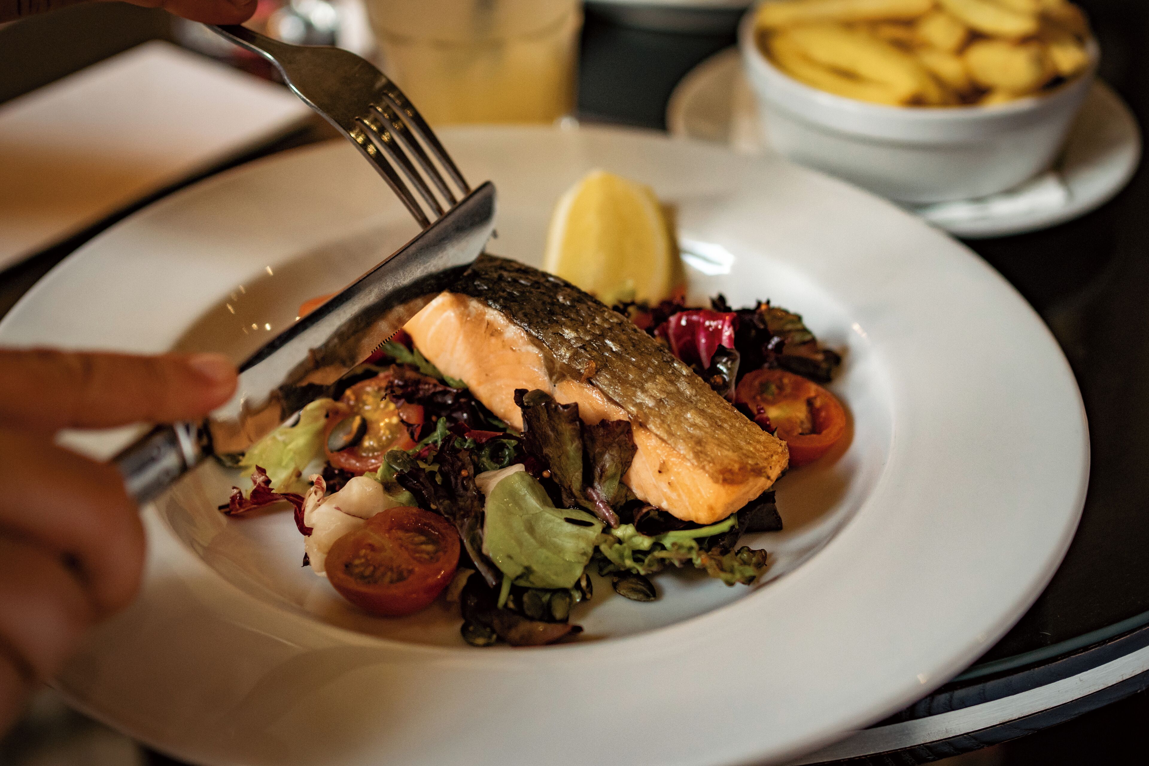Un plato de comida con salmón, ensalada y una cuña de limón.