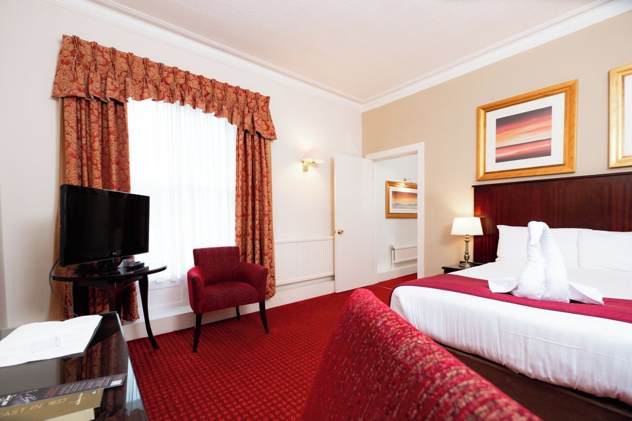 Una habitación de hotel con cama, televisor, sillón rojo y alfombra roja.