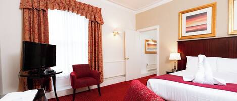 A hotel room with a bed, a TV, a red armchair, and a red carpet.