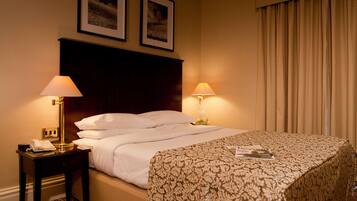 A hotel room with a bed, two bedside lamps, a nightstand with a telephone, and two framed pictures on the wall.