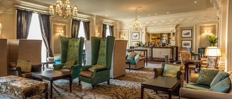 A spacious lobby with a bar area, green armchairs, and a patterned carpet.