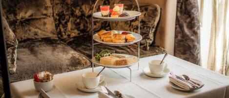 A three-tiered dessert stand with pastries and a cup of tea on a table in a room with a patterned sofa.