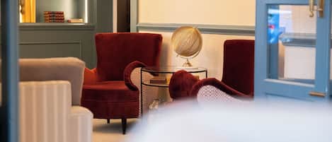 A hotel room with a red armchair, a small round table with a globe, a bookshelf with books, and a painting on the wall.