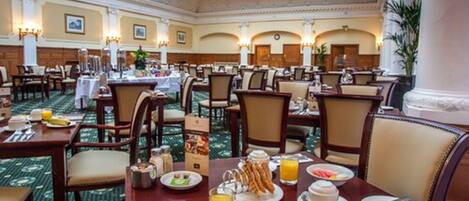 A hotel dining area with multiple tables set for breakfast, featuring plates of food, drinks, and breakfast items.