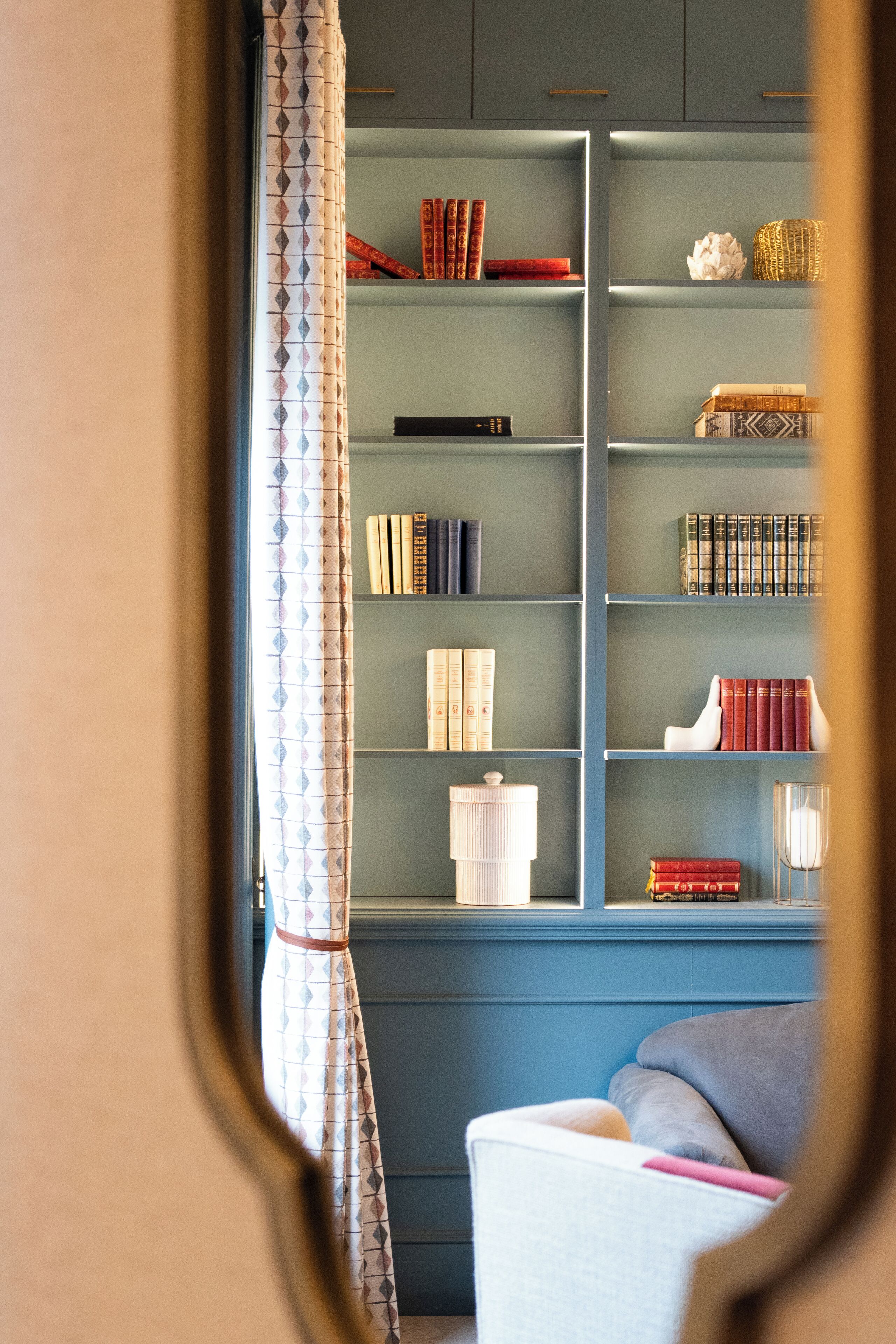 Una habitación con pared azul y una estantería llena de libros y adornos.