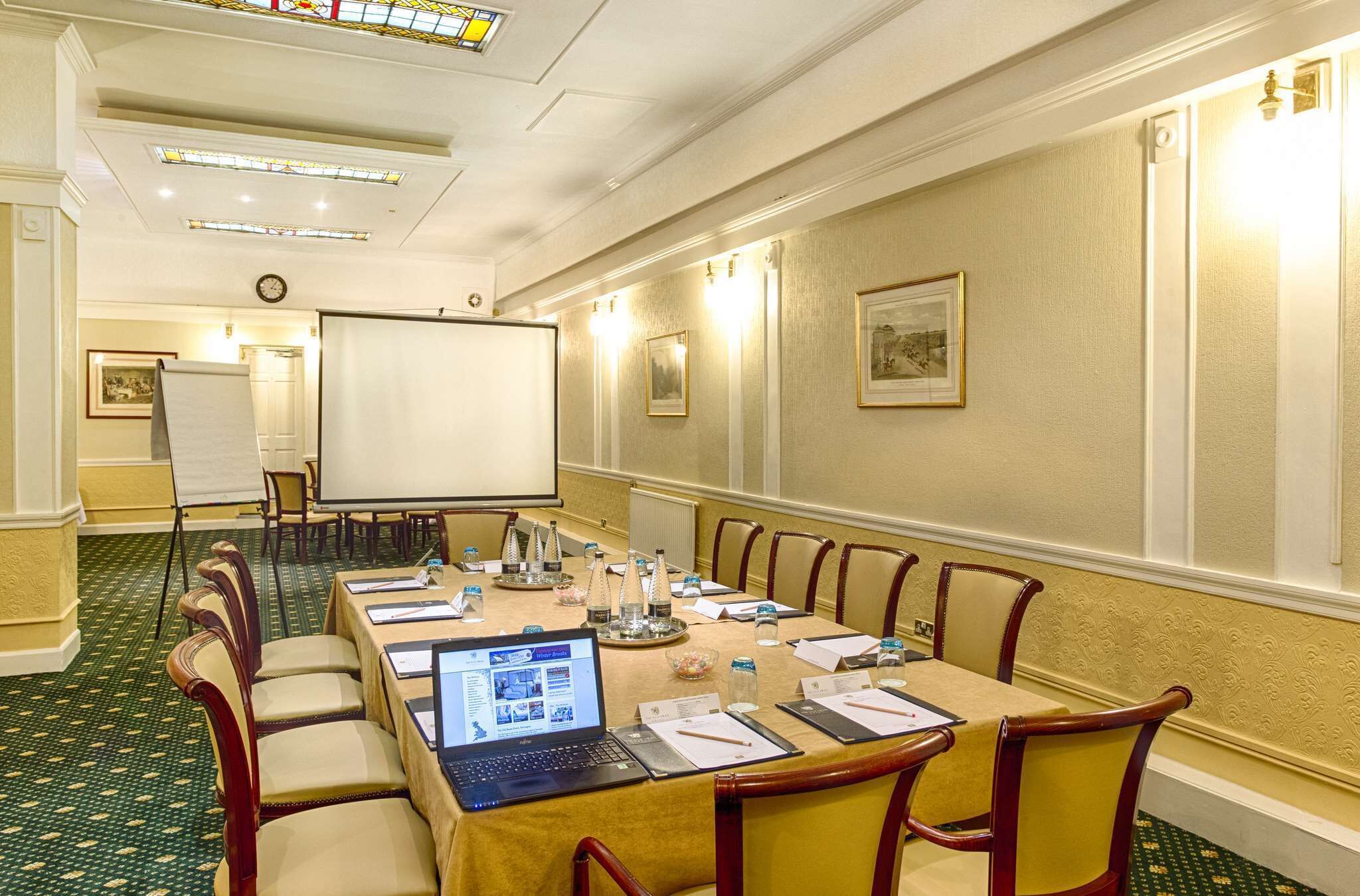 A conference room with a long table, chairs, a projector screen, and a laptop.