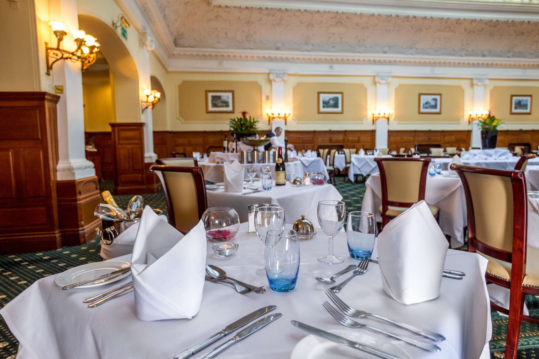 A banquet hall with tables set for a formal event, featuring chandeliers, framed artwork, and a carpeted floor.
