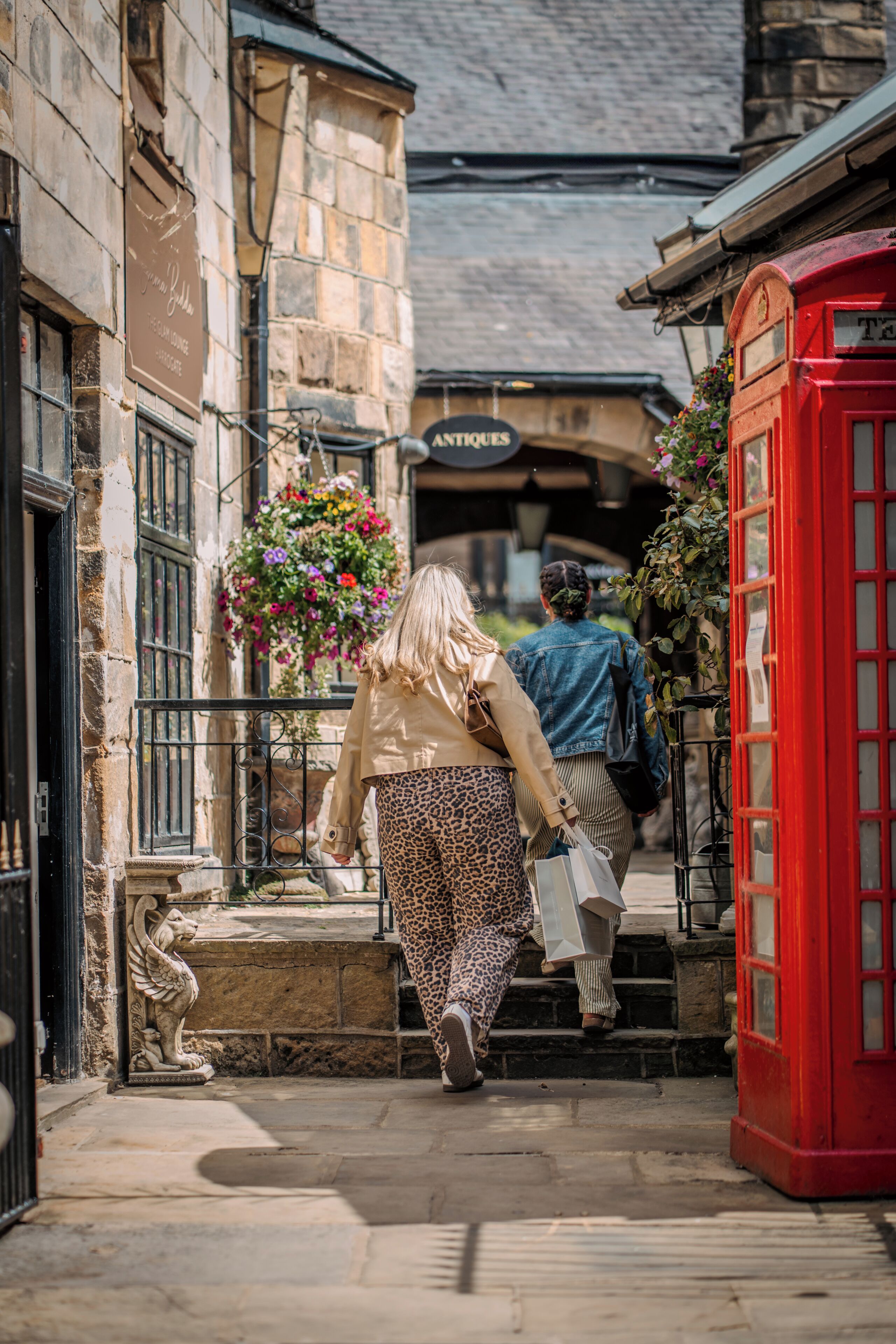 A narrow street with stone buildings, a red telephone booth, and a hanging flower basket.