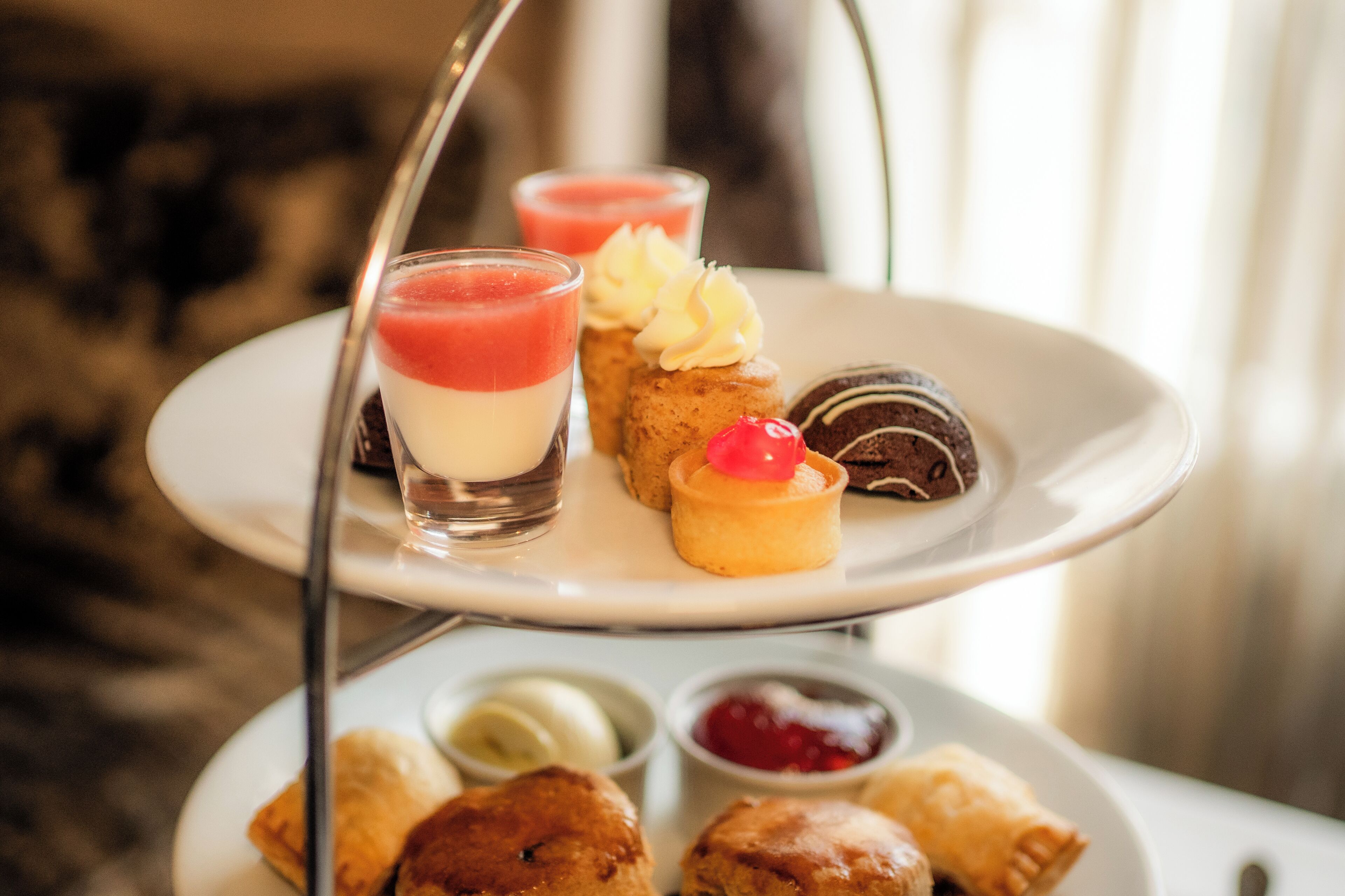 A three-tiered dessert tray with various pastries and a glass of red beverage.