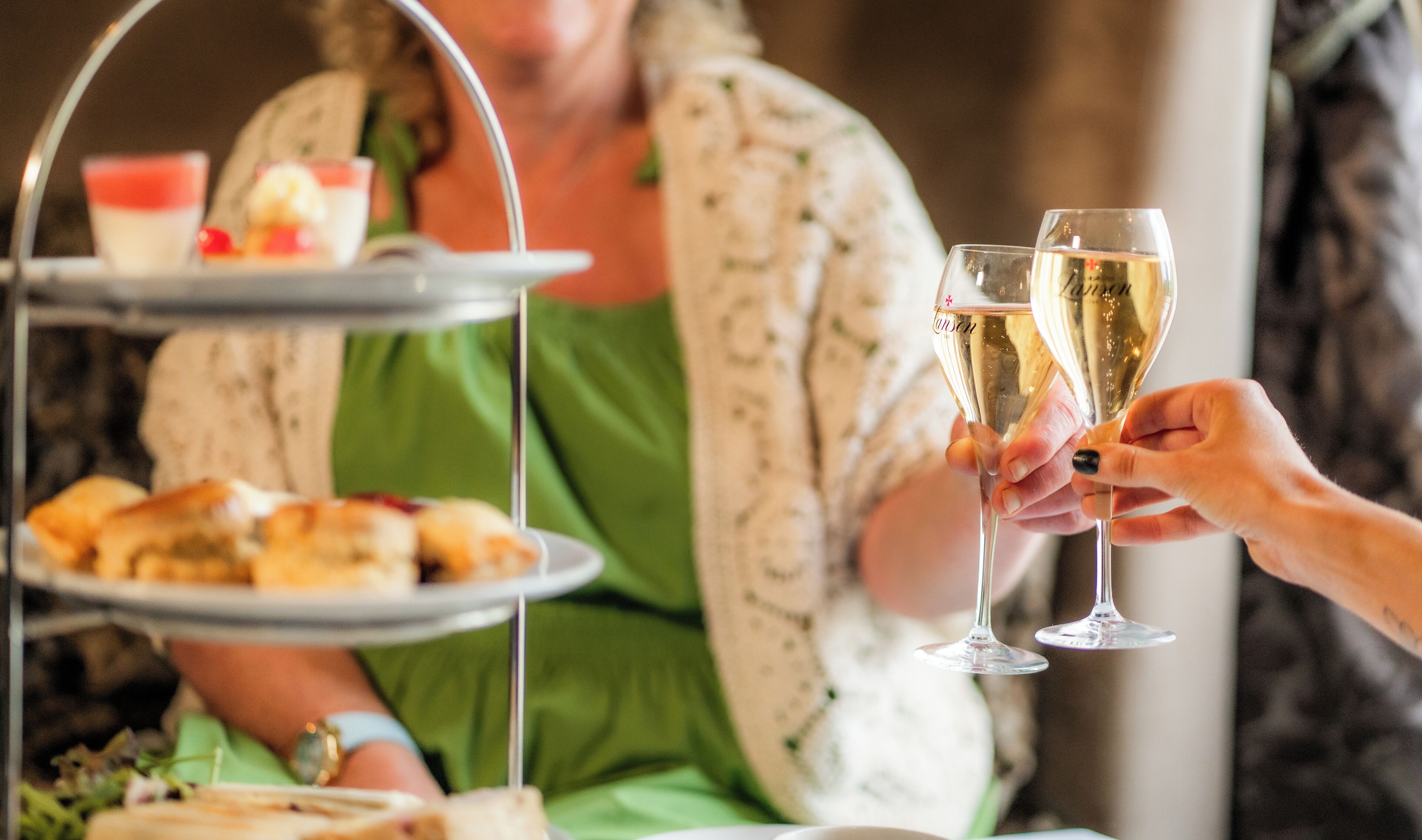 A person seated at a table with a tray of pastries and a glass of champagne.