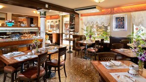 A restaurant with multiple dining tables and chairs, a buffet area with various food items, and a bar. - Hotel Ambassador Tre Rose (Venice)
