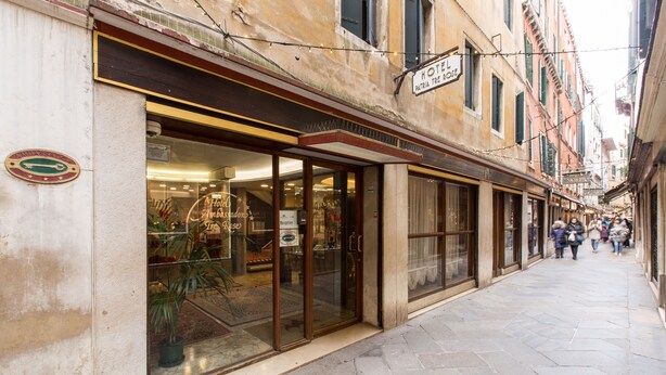 A hotel with a glass storefront, a sign reading "HOTEL PATRIA TRE," and a cobblestone street. - Hotel Ambassador Tre Rose (Venice)