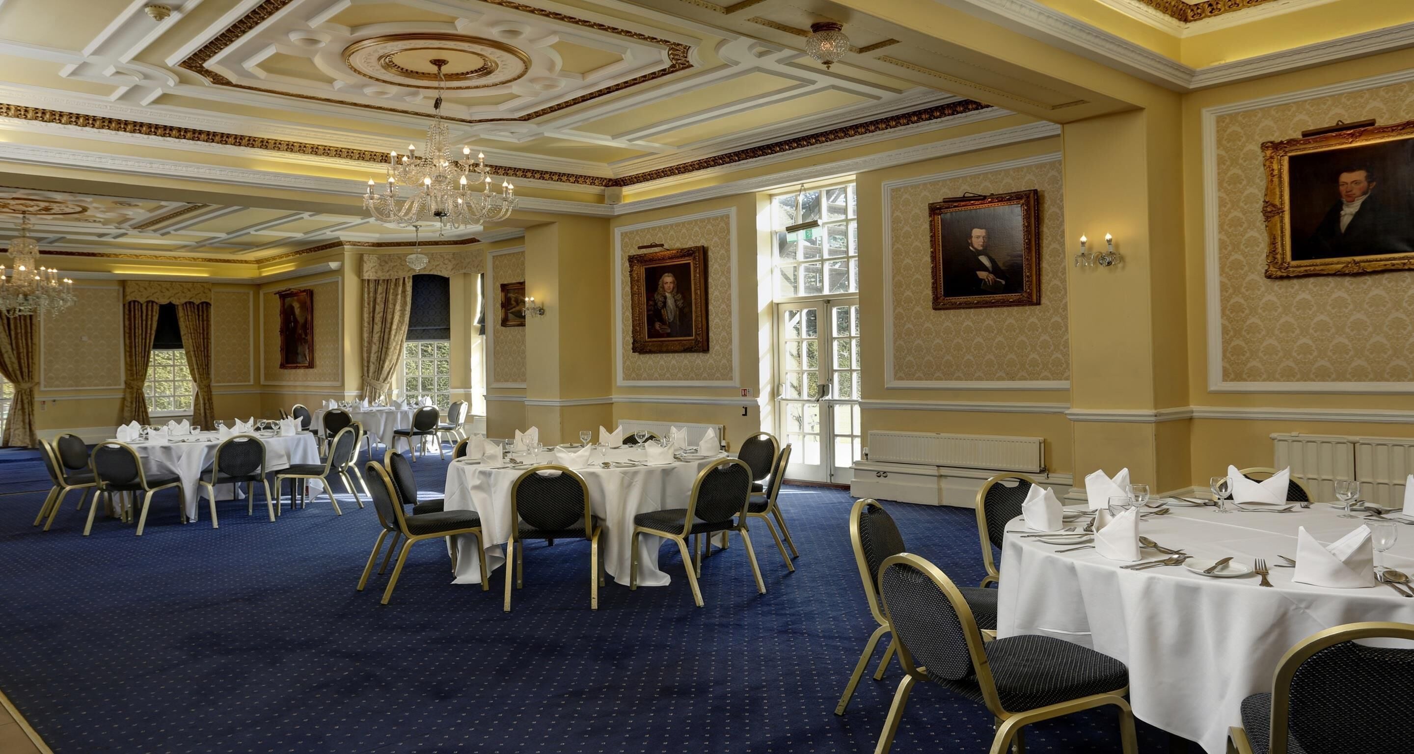 A formal dining room with multiple tables set for a banquet, chandeliers, and classical wall decorations.