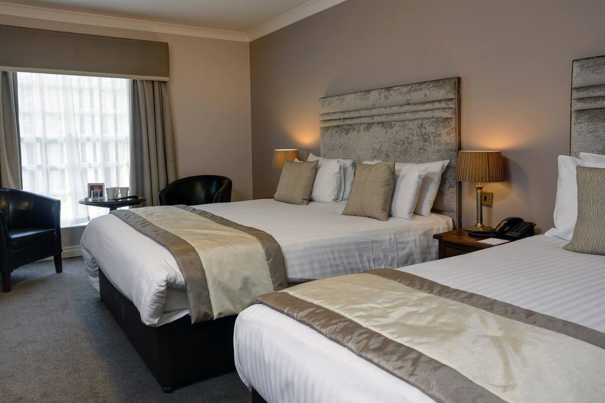A hotel room with two beds, a desk, a chair, and a large window with curtains.