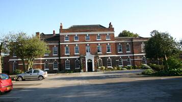 A large brick building with a central entrance, multiple windows, and a parking lot in front.