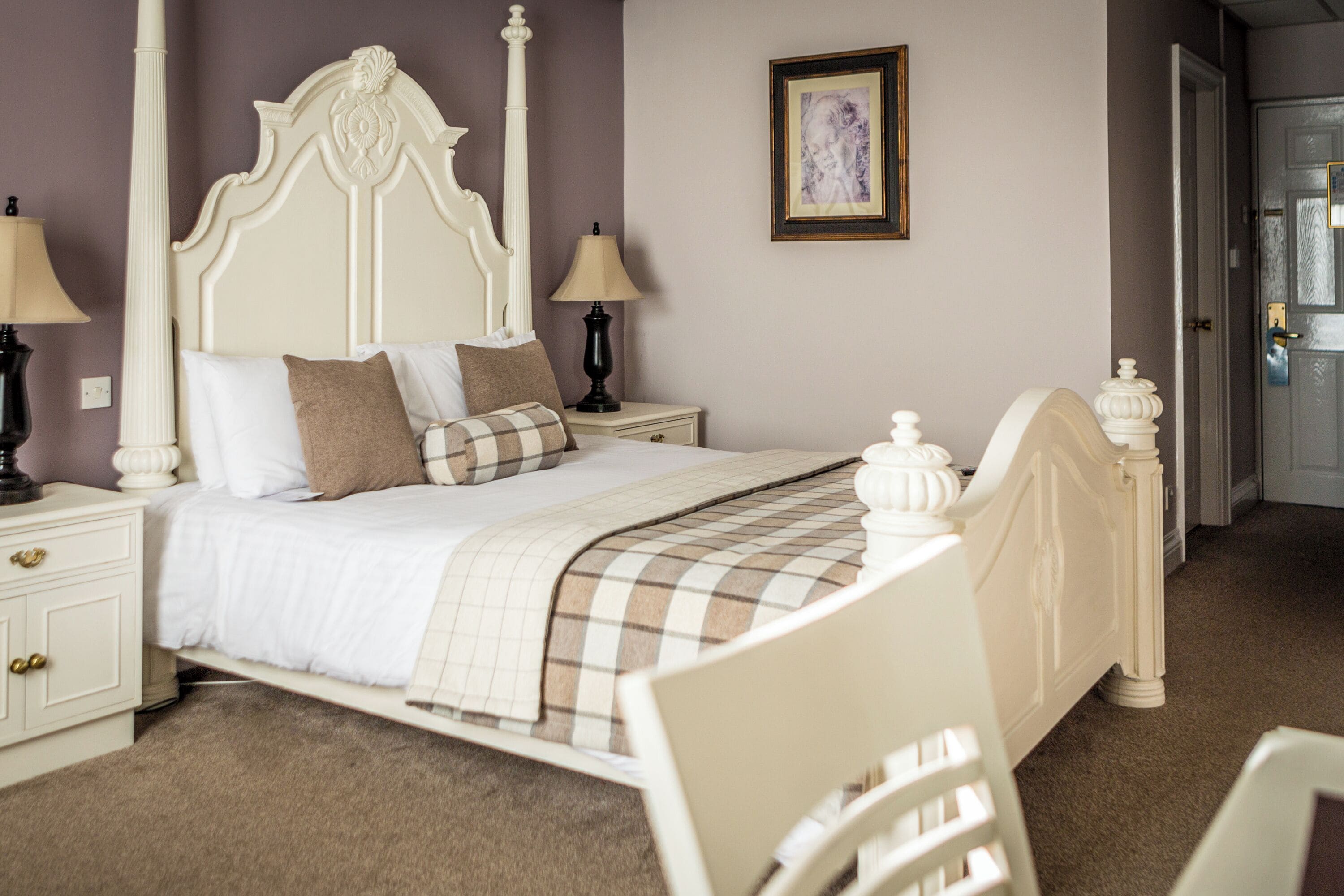 A bedroom with a bed, nightstands, a lamp, a picture on the wall, and a door.
