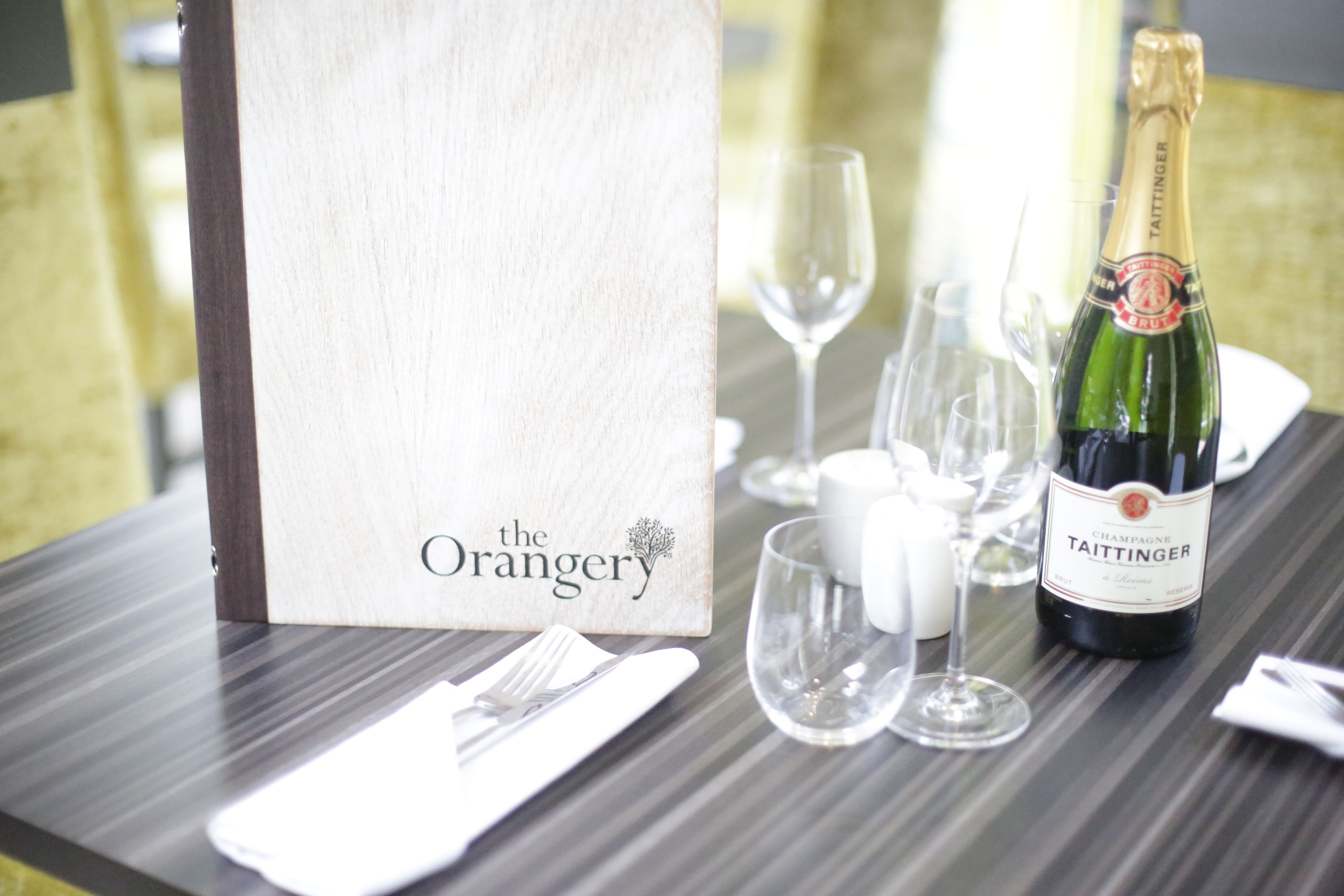 A table set with a bottle of Taittinger champagne, a white napkin, a glass, and a menu stand.