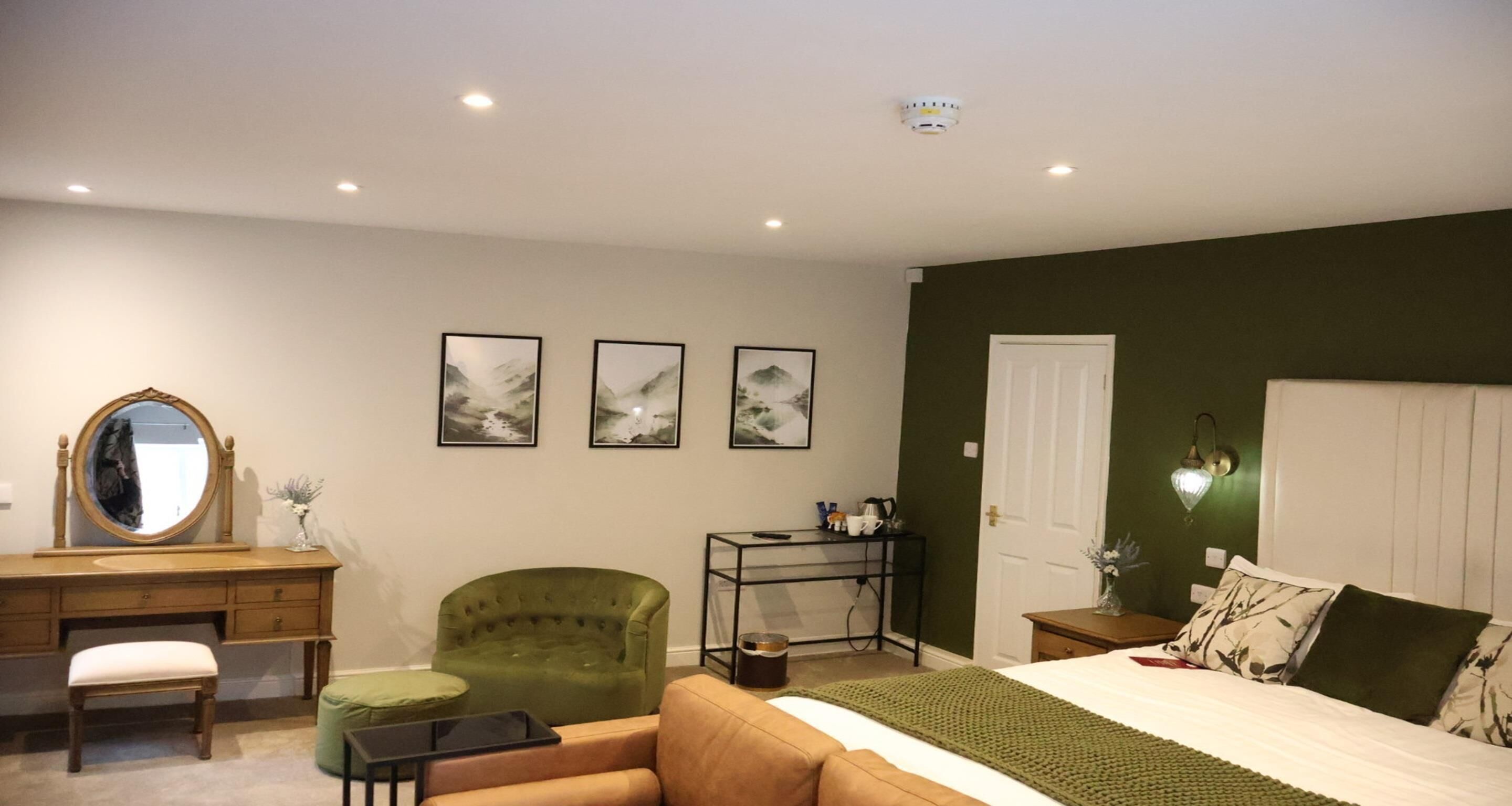 Une chambre à coucher avec un lit, un fauteuil vert, une commode en bois, un bureau et un miroir.