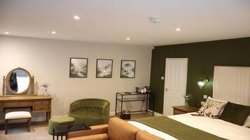 Une chambre à coucher avec un lit, un fauteuil vert, une commode en bois, un bureau et un miroir.