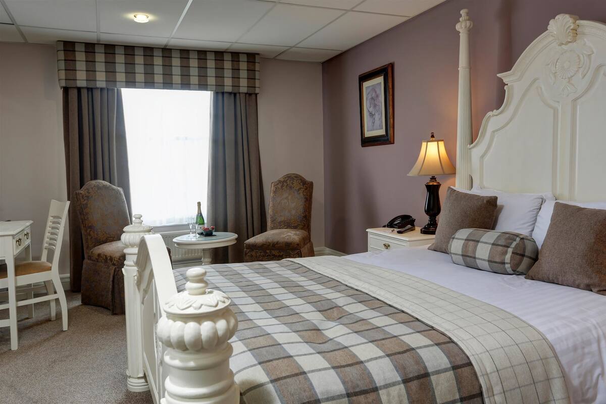 A hotel room with a large bed, two chairs, a small table, and a lamp.