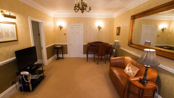 A room with a television, a leather sofa, a chandelier, and a large mirror.