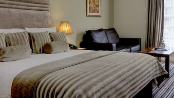 A hotel room with a large bed, a leather sofa, a bedside table, and a lamp.