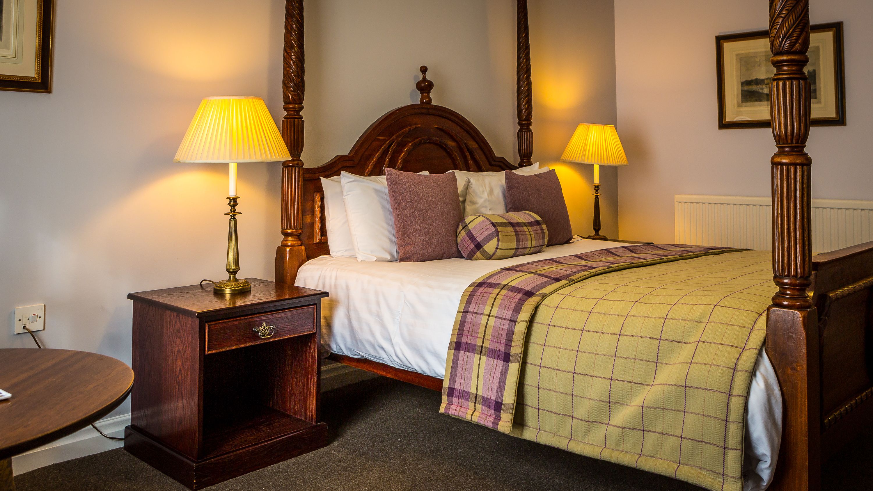 A neatly made bed with a plaid blanket, two bedside tables with lamps, and a wooden headboard.