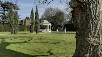 Un pabellón en un parque con césped, árboles y un edificio al fondo.