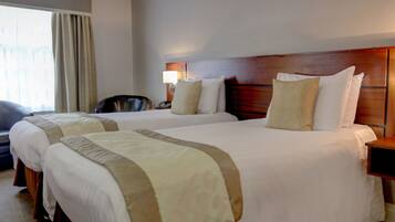 A hotel room with two beds, a desk, a chair, and a window with curtains.