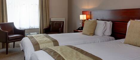 A hotel room with two beds, a chair, a lamp, and a window with curtains.
