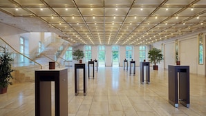 A spacious lobby with a high ceiling, a central staircase, and multiple potted plants. - Sheraton Offenbach Hotel (Offenbach am Main)