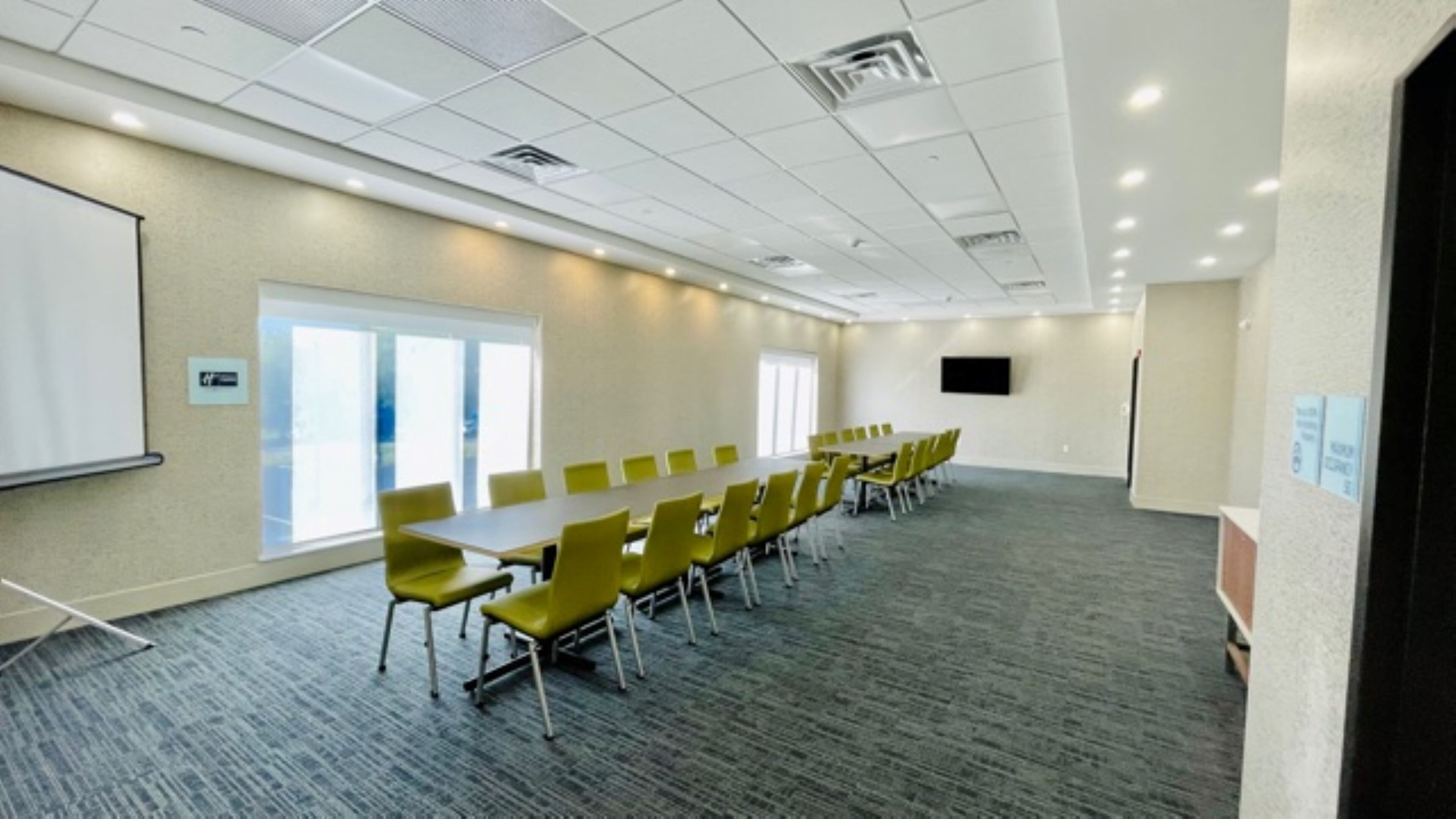 A conference room with a long table, yellow chairs, a whiteboard, and a large window.