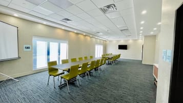 A conference room with a long table, yellow chairs, a whiteboard, and a large window.