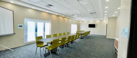 Une salle de conférence avec une longue table, des chaises jaunes, un tableau blanc et une grande fenêtre.