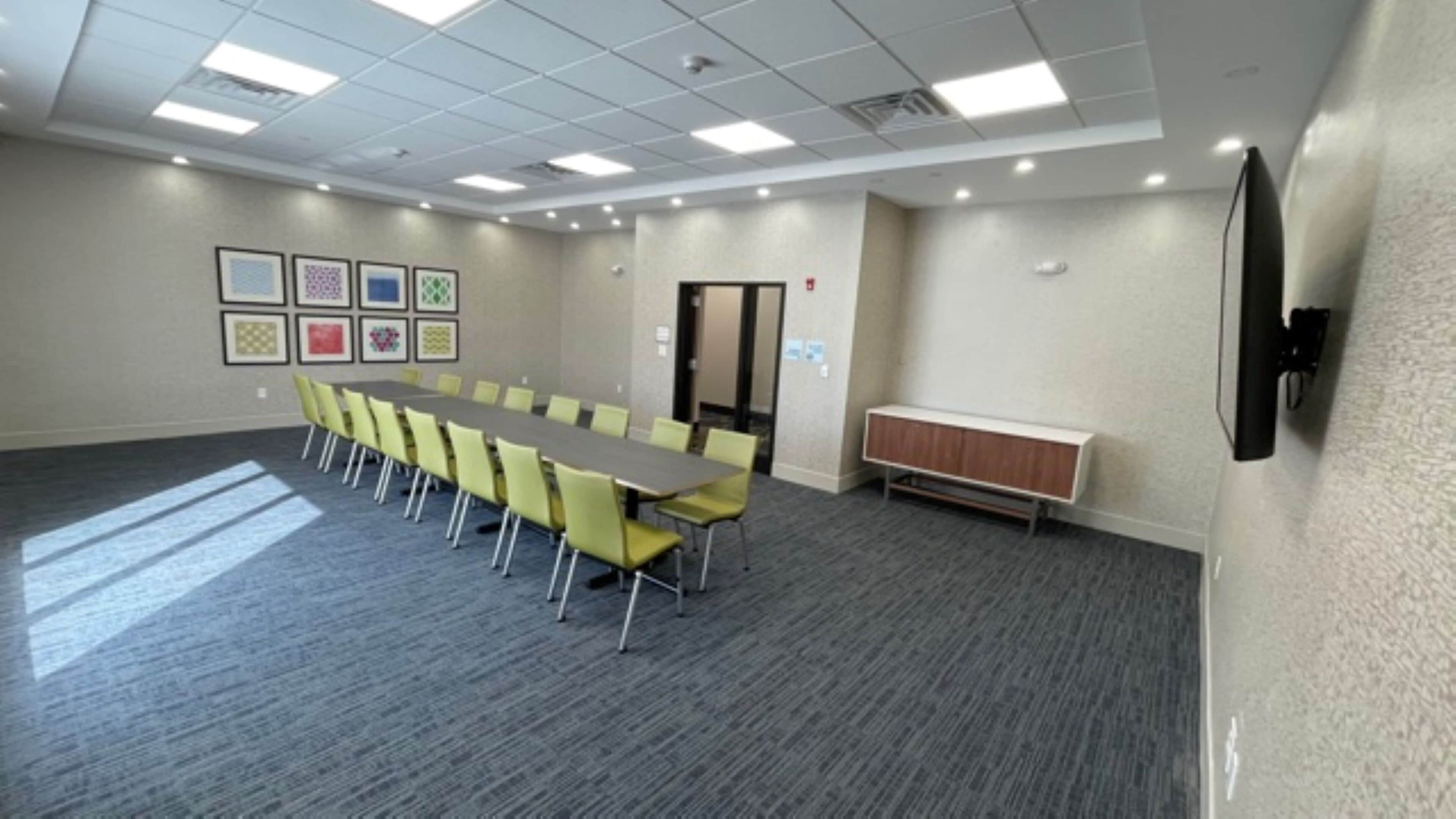 Een vergaderruimte met een lange tafel, gele stoelen, een whiteboard en een kast.
