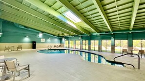 An indoor swimming pool with a curved design, surrounded by chairs and tables, and large windows allowing natural light. - Holiday Inn Express Fall River North by IHG (Fall River)