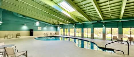 An indoor swimming pool with a curved design, surrounded by chairs and tables, and large windows allowing natural light.