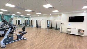 A spacious gym with cardio machines, a television mounted on the wall, and a clean, modern design.