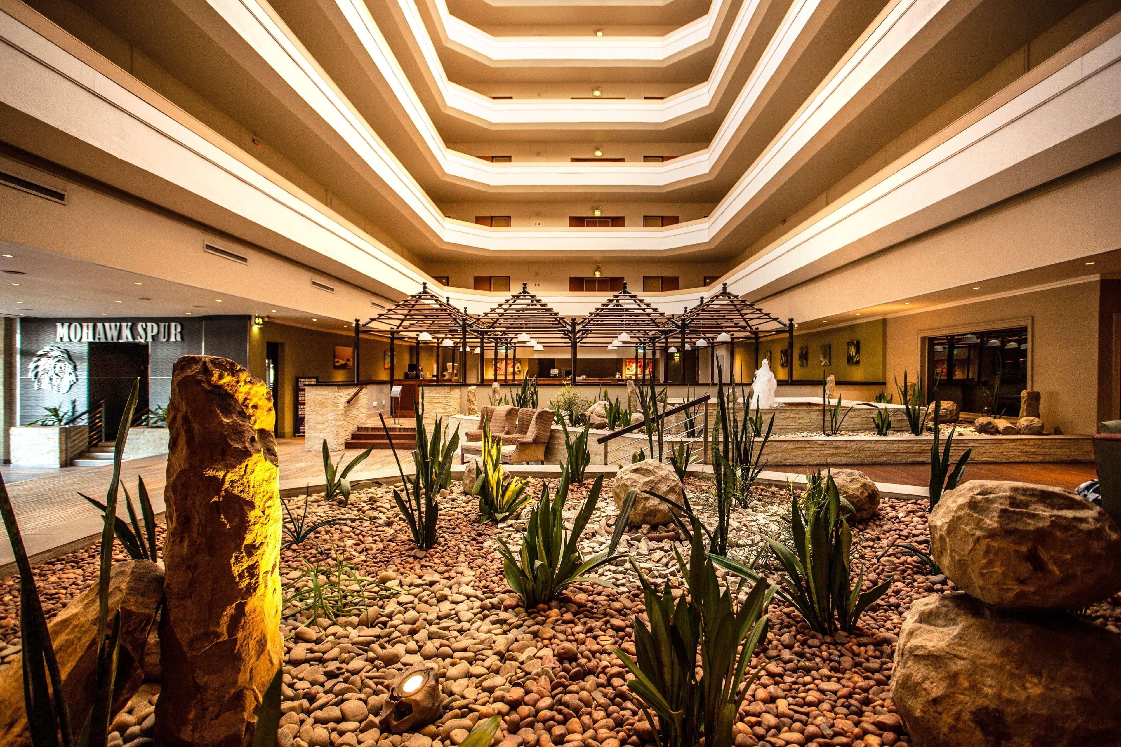 Et hotel lobby med et centralt siddeområde, en stor klippeskulptur og et moderne loftdesign.