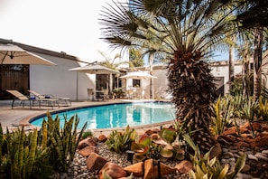 A swimming pool surrounded by rocks and plants, with lounge chairs and umbrellas.