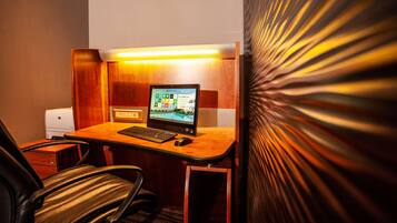 Una habitación de hotel con un escritorio de madera, una computadora portátil, una impresora y una silla.