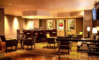 Um bar ou lounge de hotel, com balcão de bar, diversas opções de assento e uma tela de televisão.