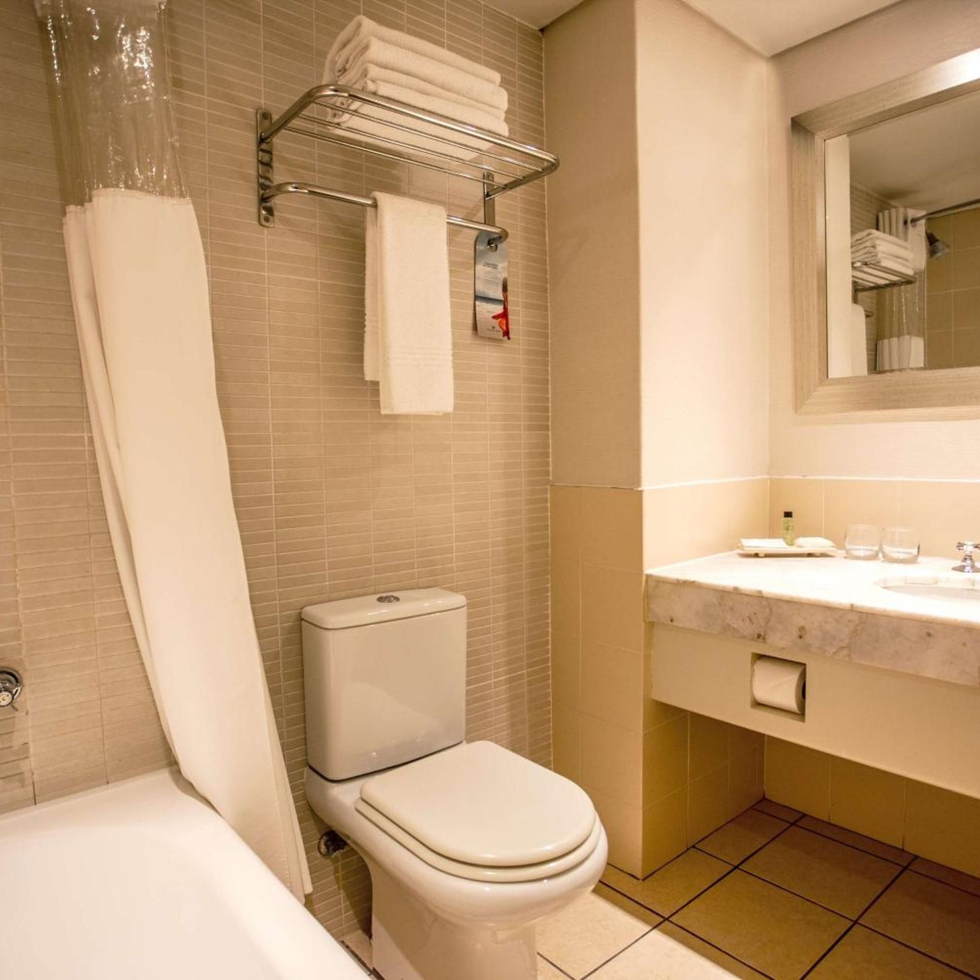 A bathroom with a toilet, a bathtub, a towel rack, and a mirror.
