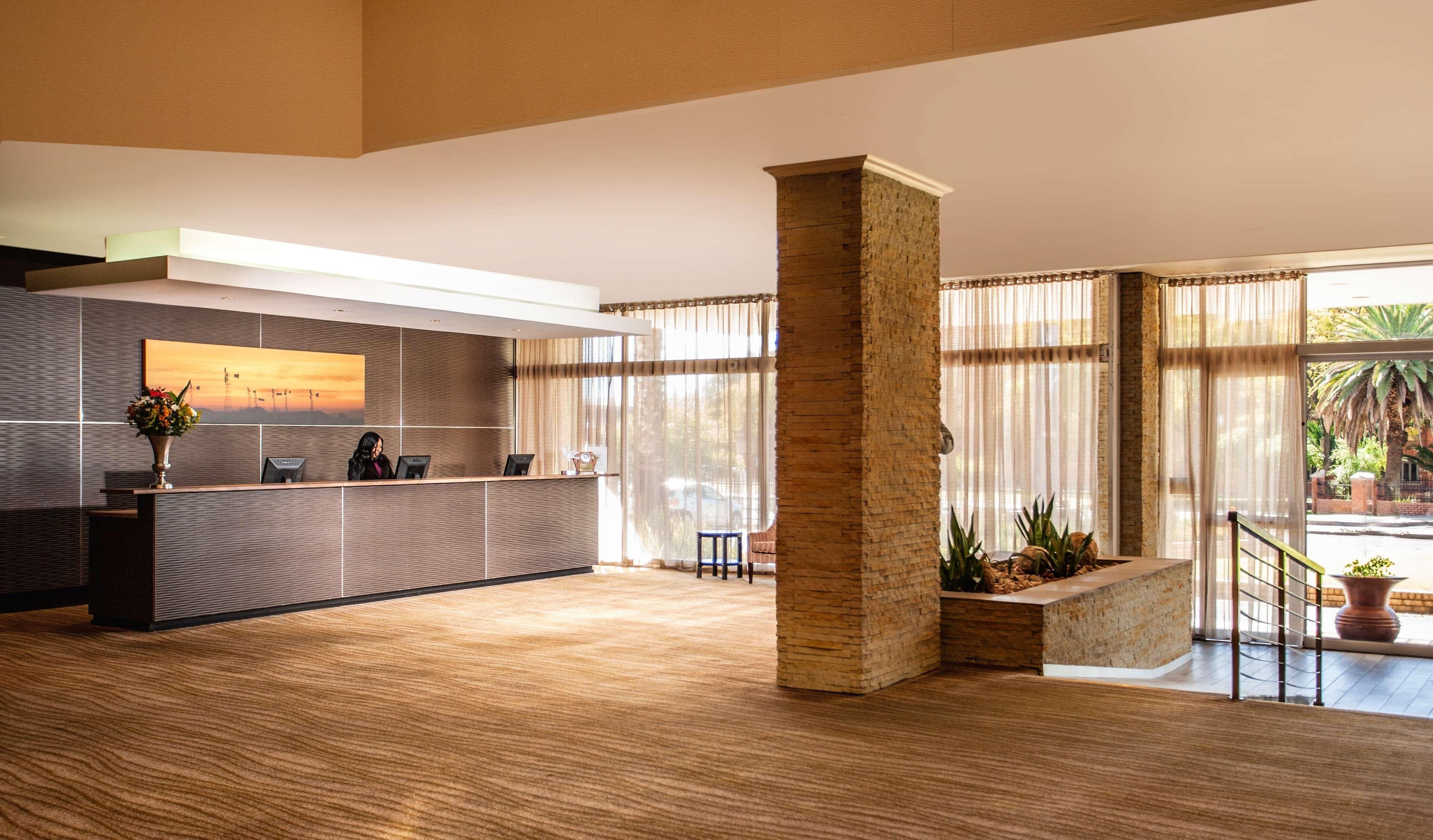 A modern reception area with a reception desk, a large window with curtains, a stone pillar, and a view of the outdoors.