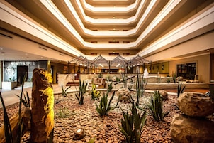 Un vestíbulo de hotel con una zona de estar central, una gran escultura de roca y un diseño de techo moderno.
