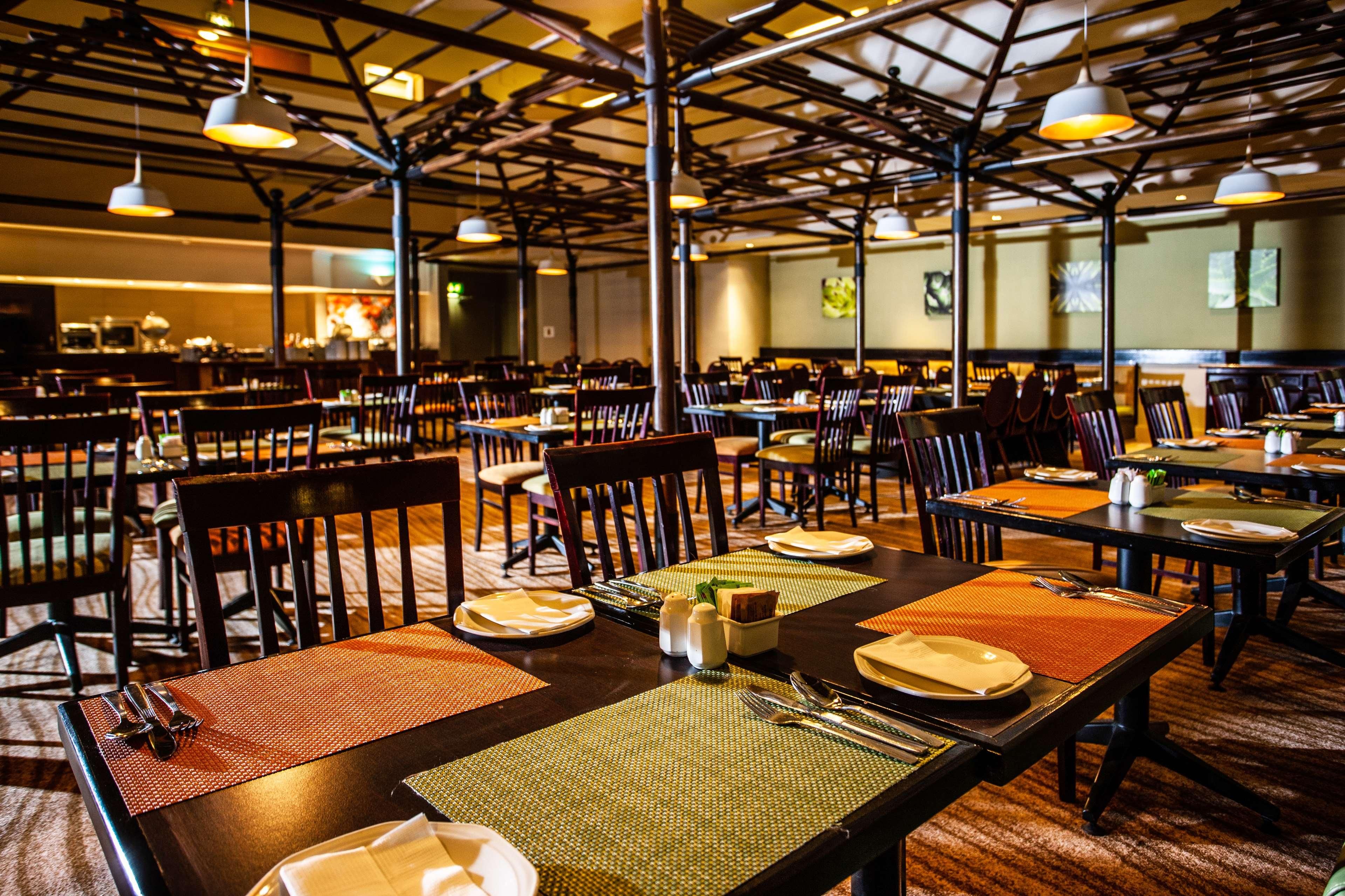 Un restaurante con varias mesas y sillas, un techo alto con vigas a la vista y lámparas colgantes.