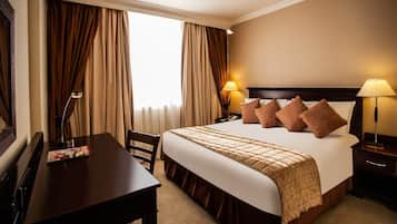 A hotel room with a bed, bedside lamps, a desk, and a chair.