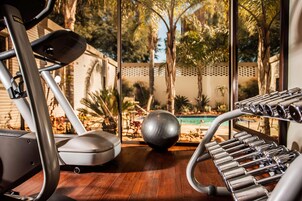 Un gimnasio con equipamiento de ejercicio, una pelota grande para hacer ejercicio y vistas a una piscina y árboles.